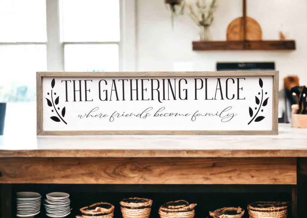 The Gathering Place where friends become family framed farmhouse sign on white shiplap wall above rustic wood console table angled view