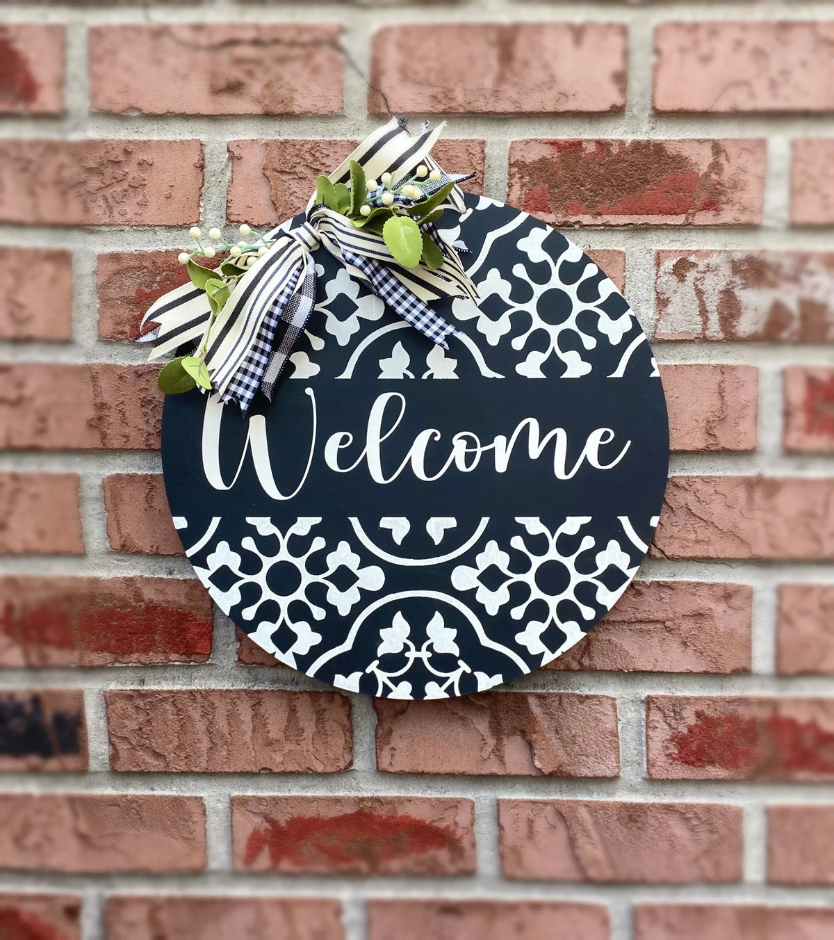 Black and white Welcome round door hanger hanging on brick wall with gingham bow