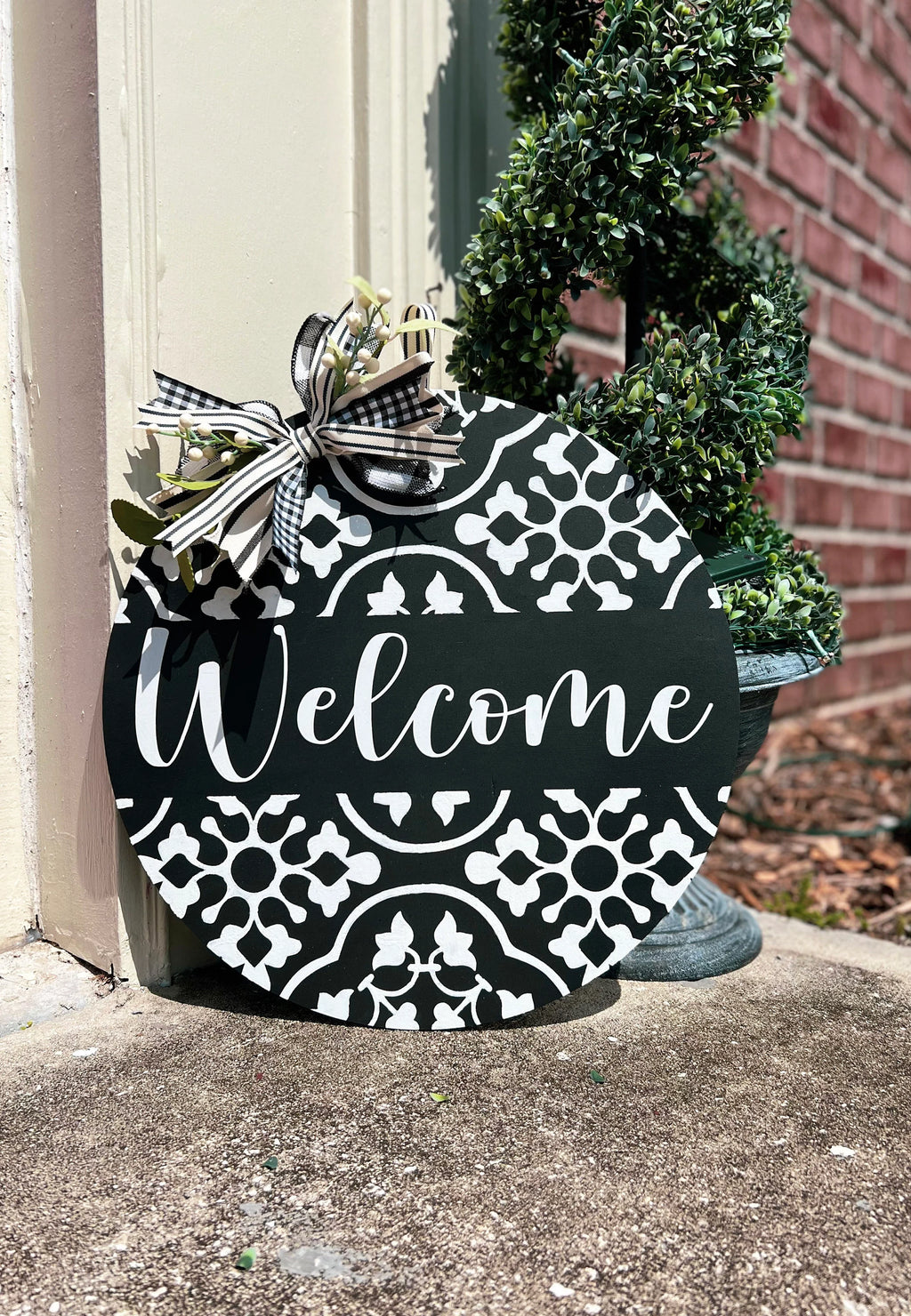 Black and white Welcome round door hanger hanging on red front door with gold knocker