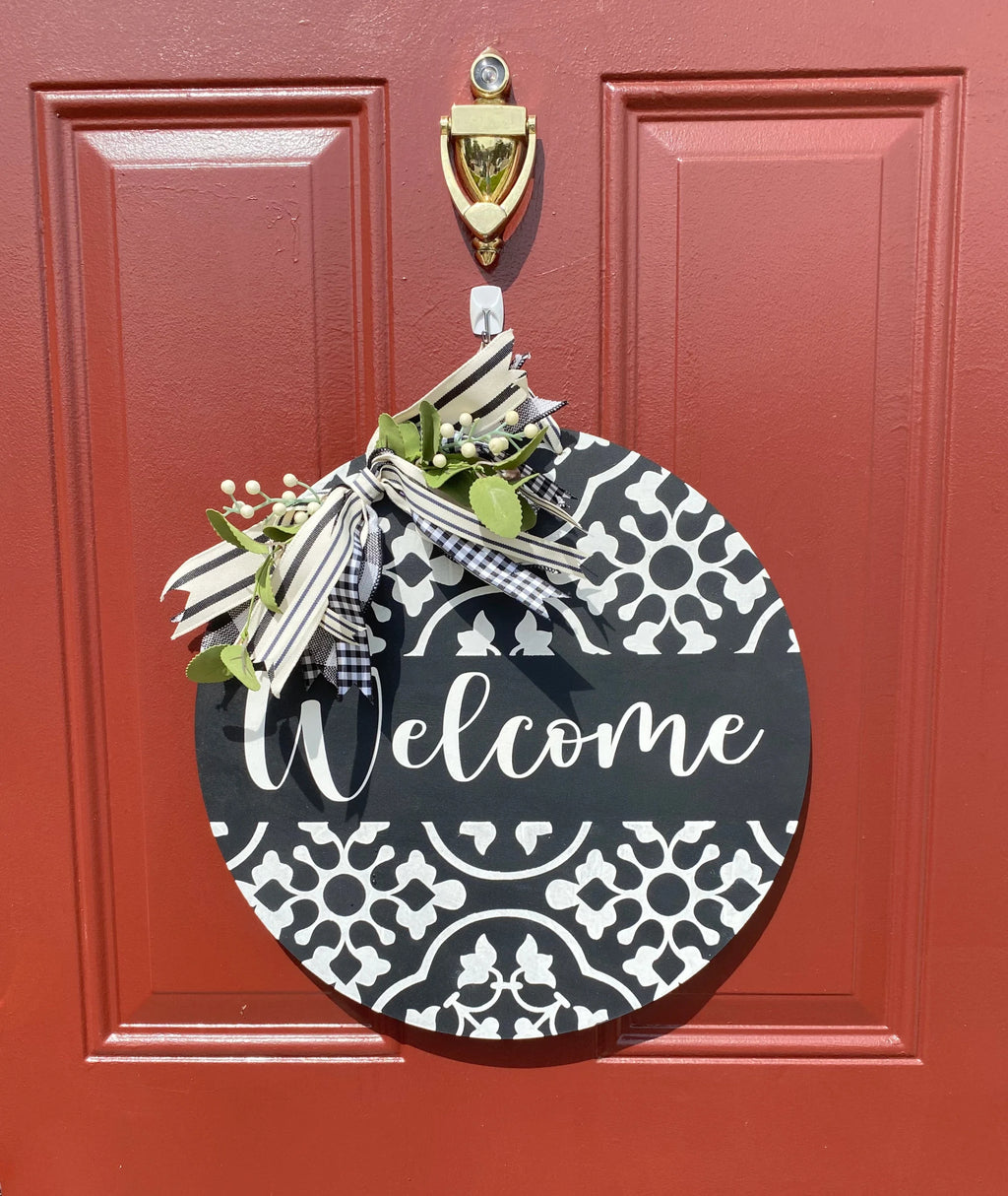 Black and white Welcome door hanger leaning on white door frame with boxwood topiary side angle