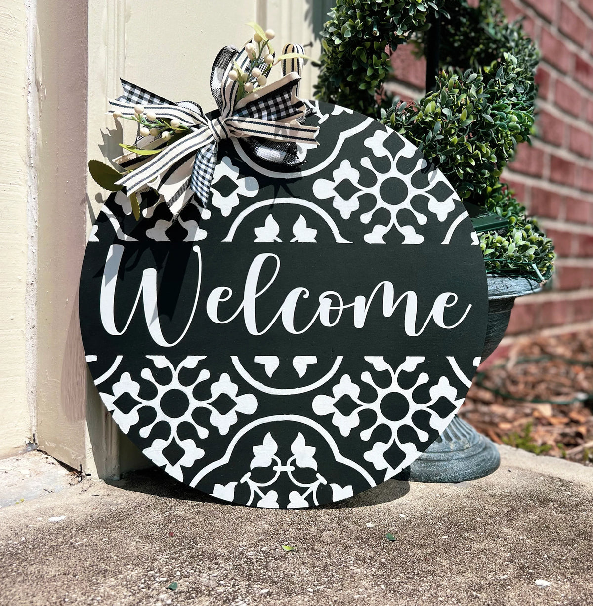 Black and white Welcome door hanger on brick wall with white berry and greenery bow