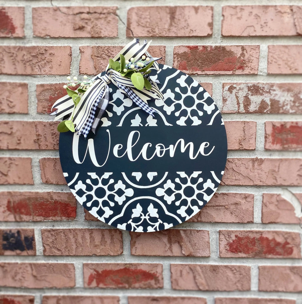 Black and white Welcome door hanger leaning on porch with boxwood topiary close-up