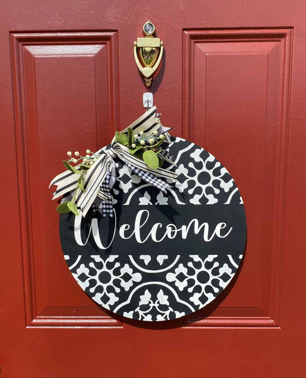 Black and white Welcome door hanger on brick wall angled view with white berry bow