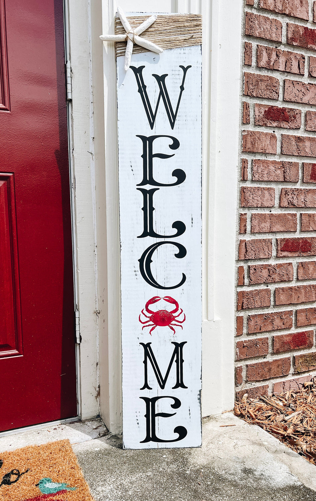 Crab Welcome porch leaner full view leaning against red front door with brick wall