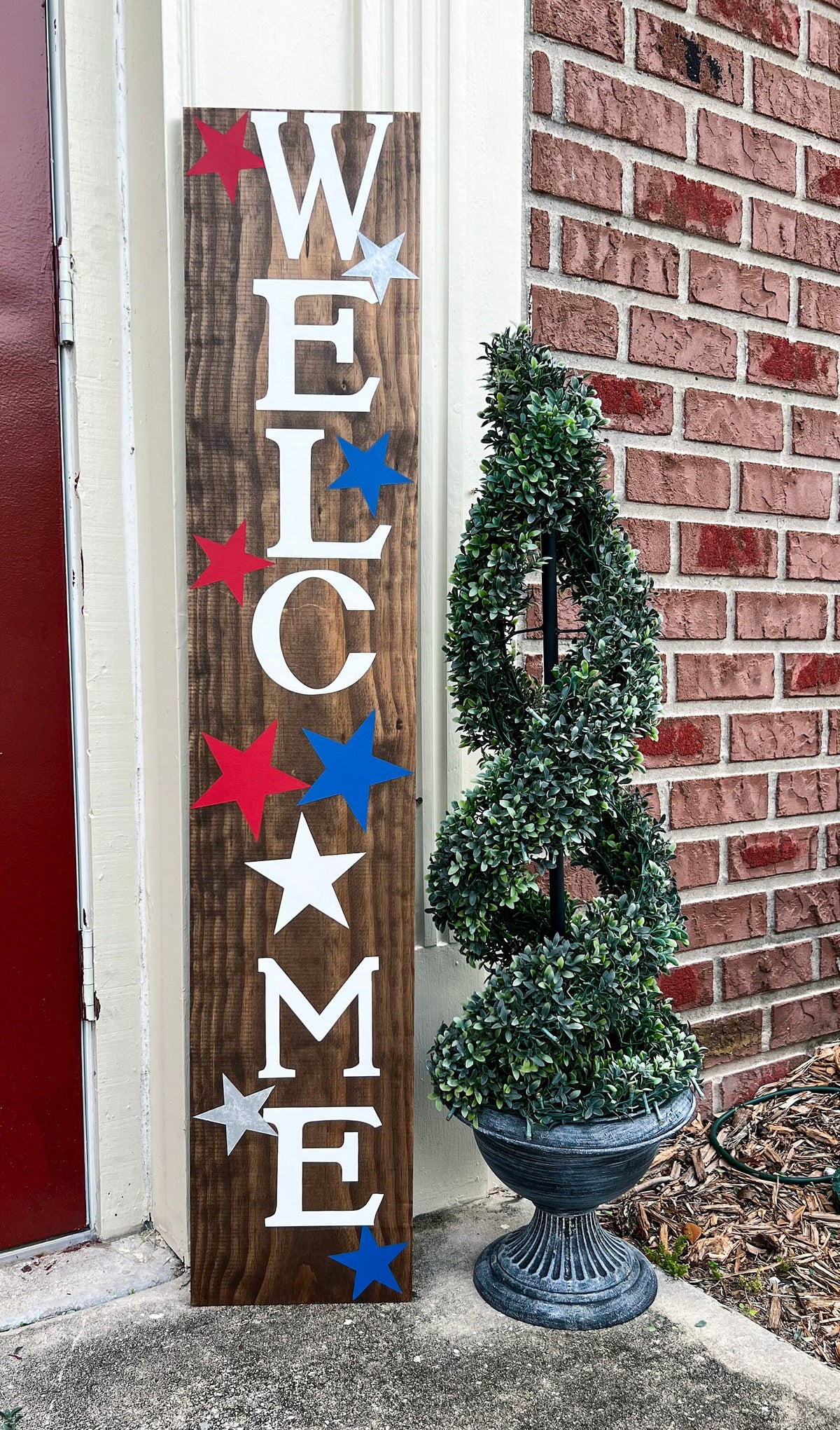 Handpainted Welcome porch leaner sign with red white and blue stars on dark walnut stained white pine board leaning against red door wide shot