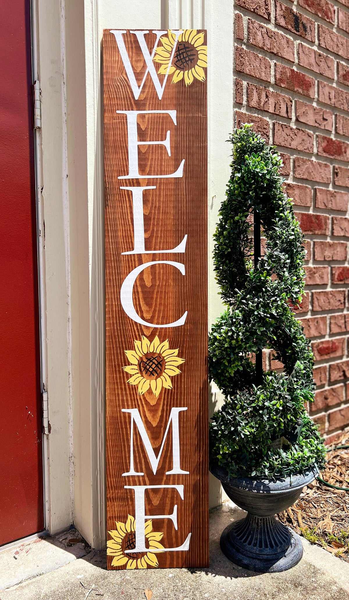 Handpainted Welcome porch leaner with yellow sunflowers on dark walnut stained white pine leaning against white door frame angled view