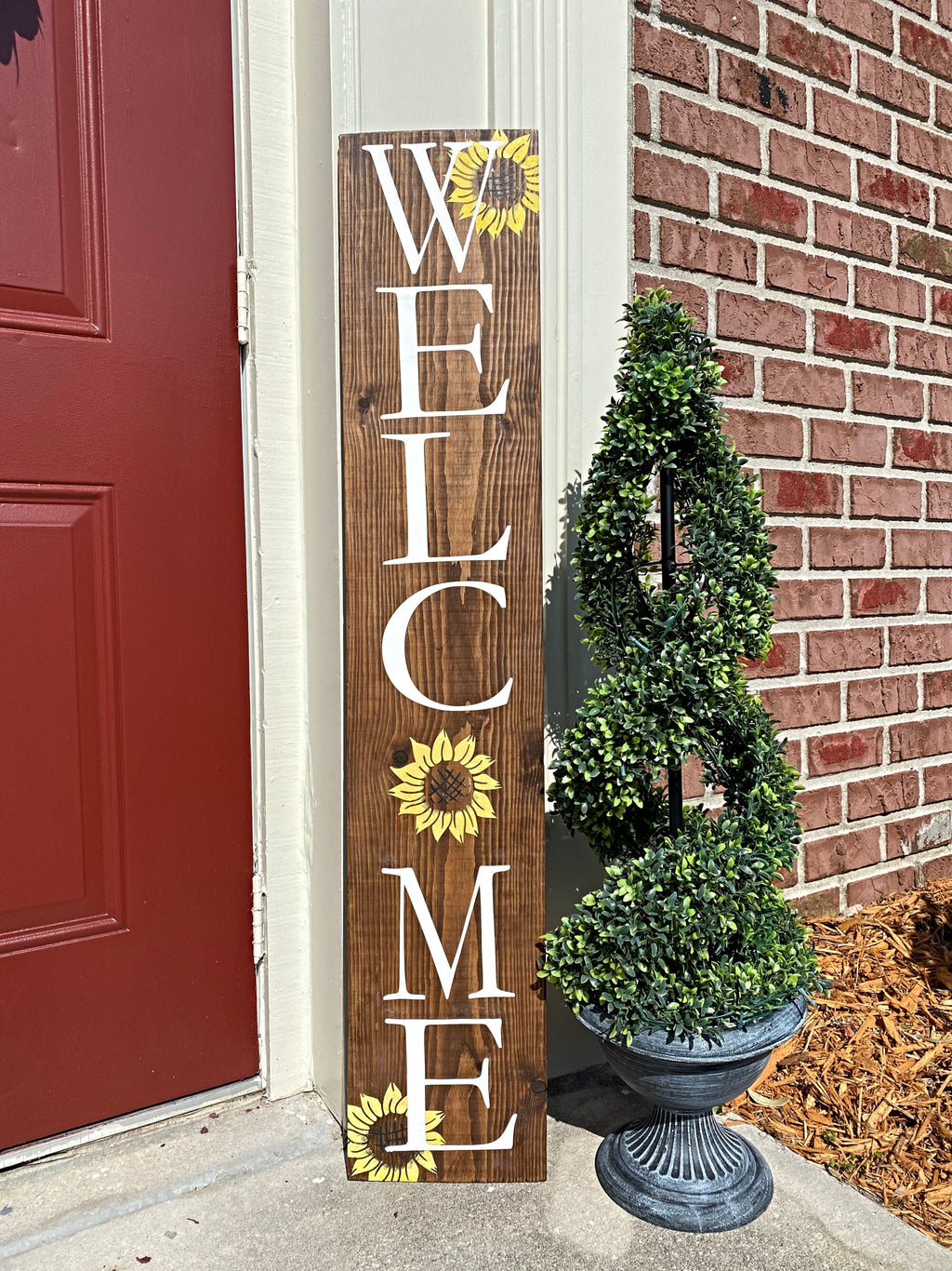 Handpainted Welcome porch leaner with yellow sunflowers on dark walnut stained white pine leaning against red door with boxwood topiary close up