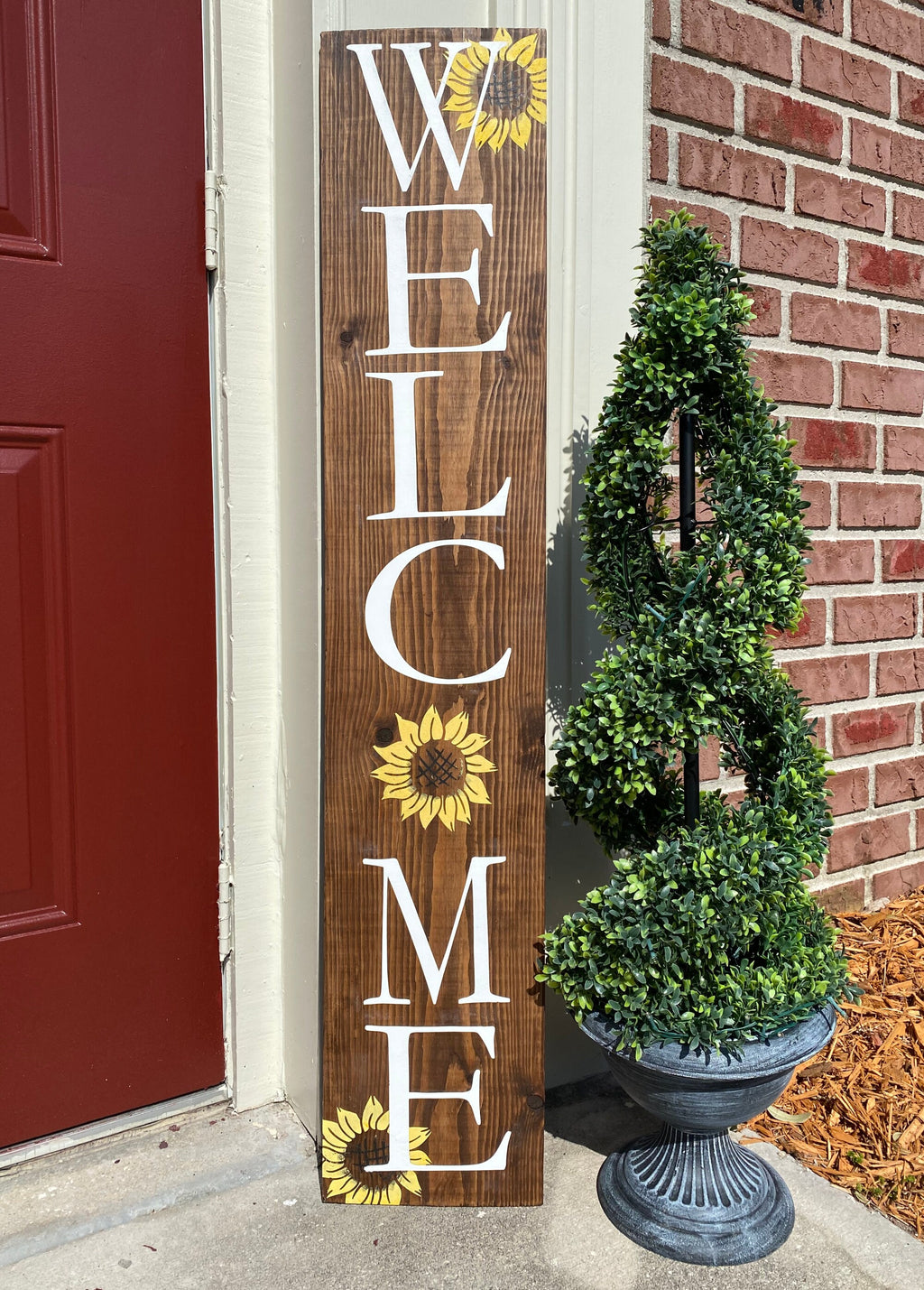 Handpainted Welcome porch leaner with yellow sunflowers on dark walnut stained white pine leaning against white door frame with boxwood topiary close up