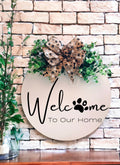 Welcome To Our Home paw print birch wood door hanger with eucalyptus and paw print bow on brick wall