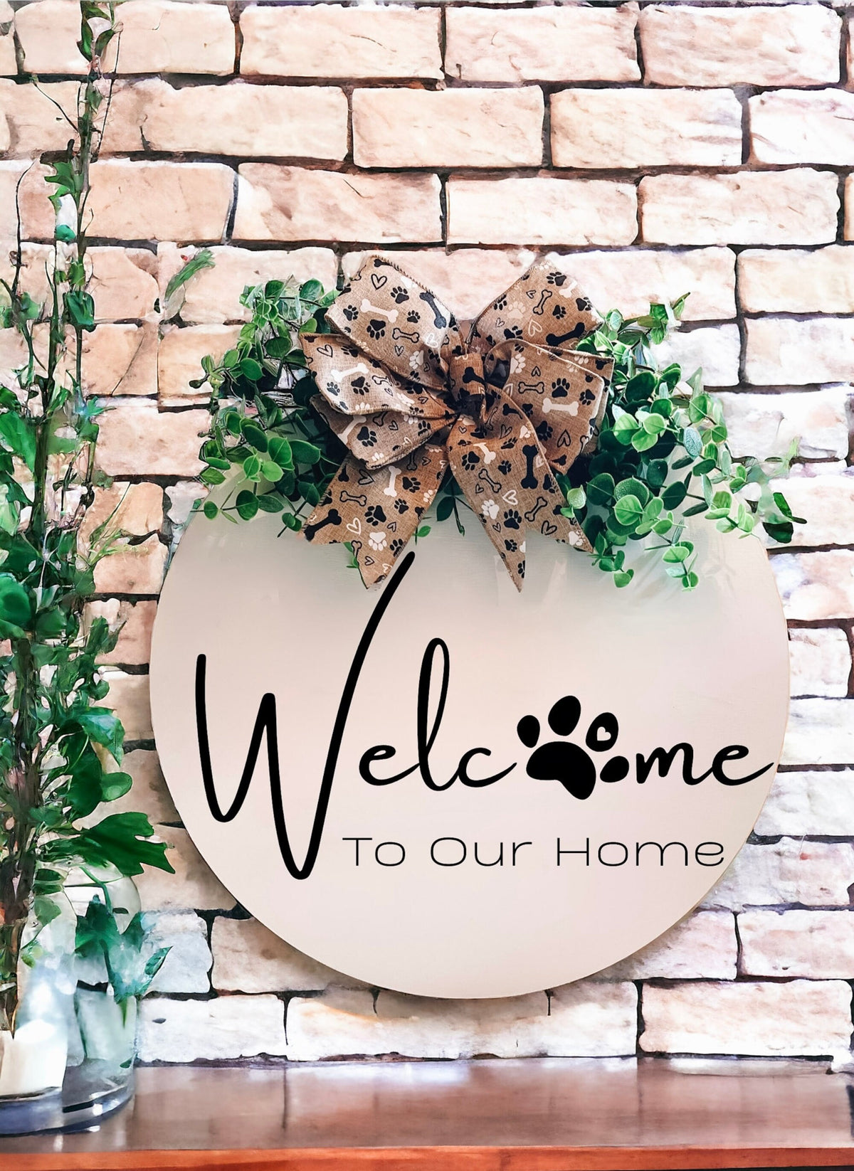 Welcome To Our Home paw print birch wood door hanger with eucalyptus and paw print bow on brick wall